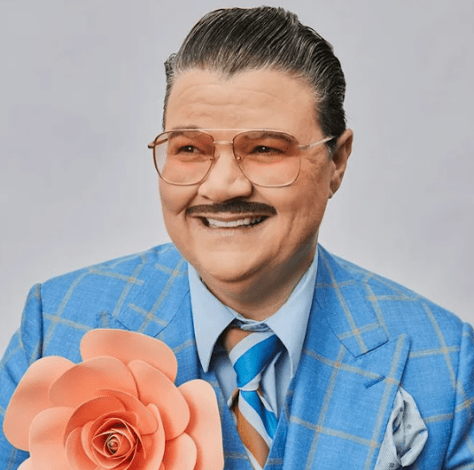 Photo of Murray Hill in a blue plaid jacket and holding a large flower.