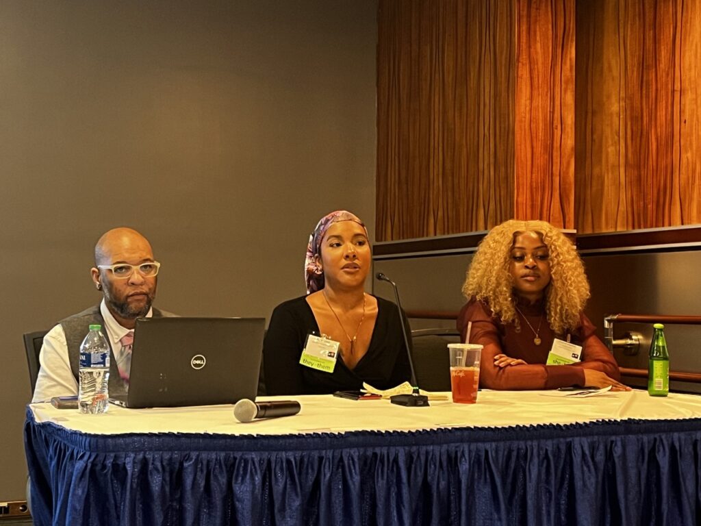 three Black people sitting at a table. two are female presenting, one is masculine presenting.