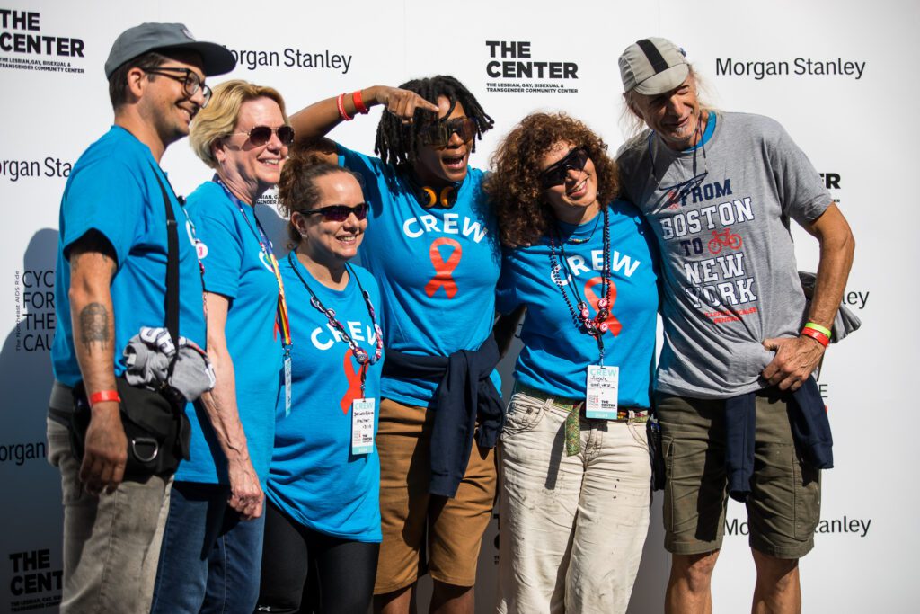 six people pose. 5 are wearing blue tee shirts with the word CREW written on it in white capital letters one is wearing a gray shirt tee shirt they all pose in front of a backdrop with The Center, Morgan Stanley logos