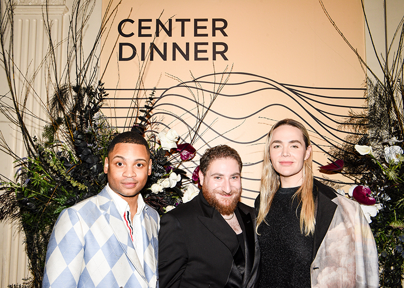 three people standing together smiling in front of a backdrop that says Center Dinner