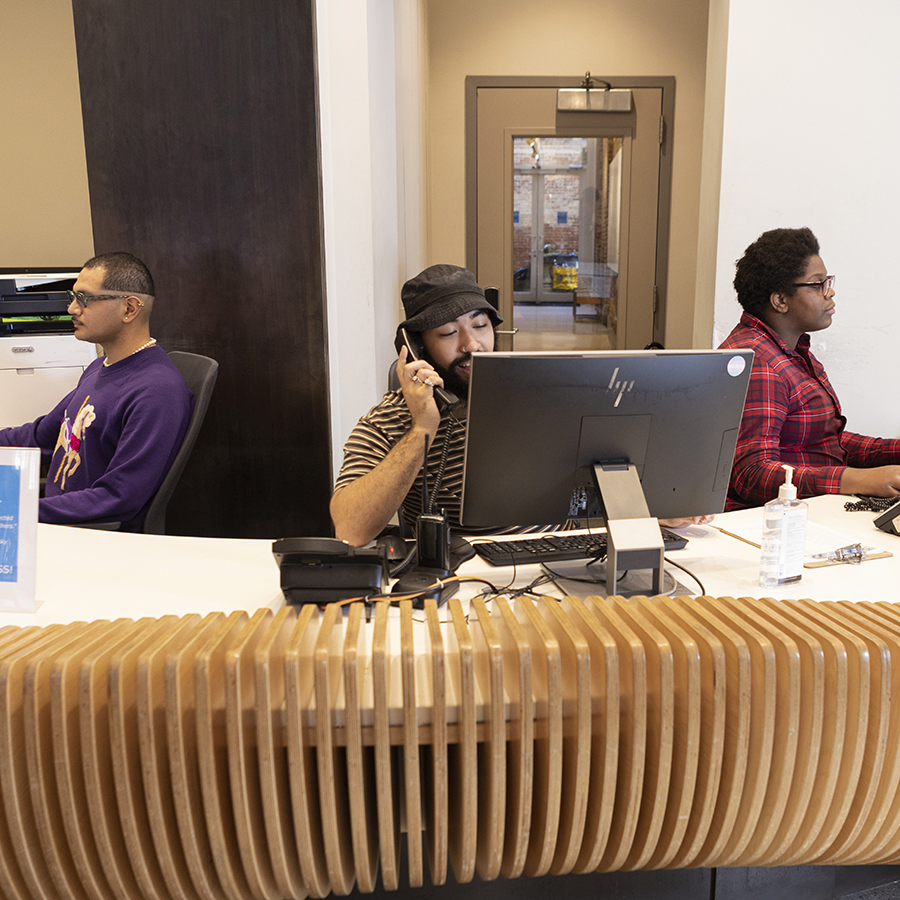 three people at the front desk working on computers and talking on the phone