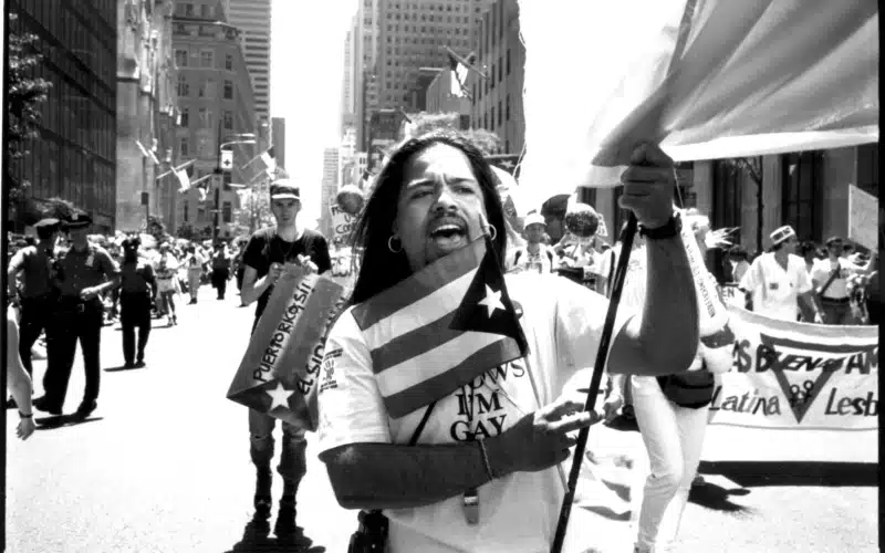 a black and white photo of a marcher in the pride march holding a puerto rico flag