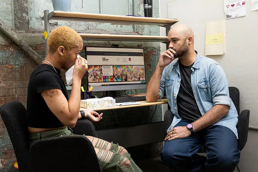 Two people having a conversation the person on the right is using a tissue to wipe their eye