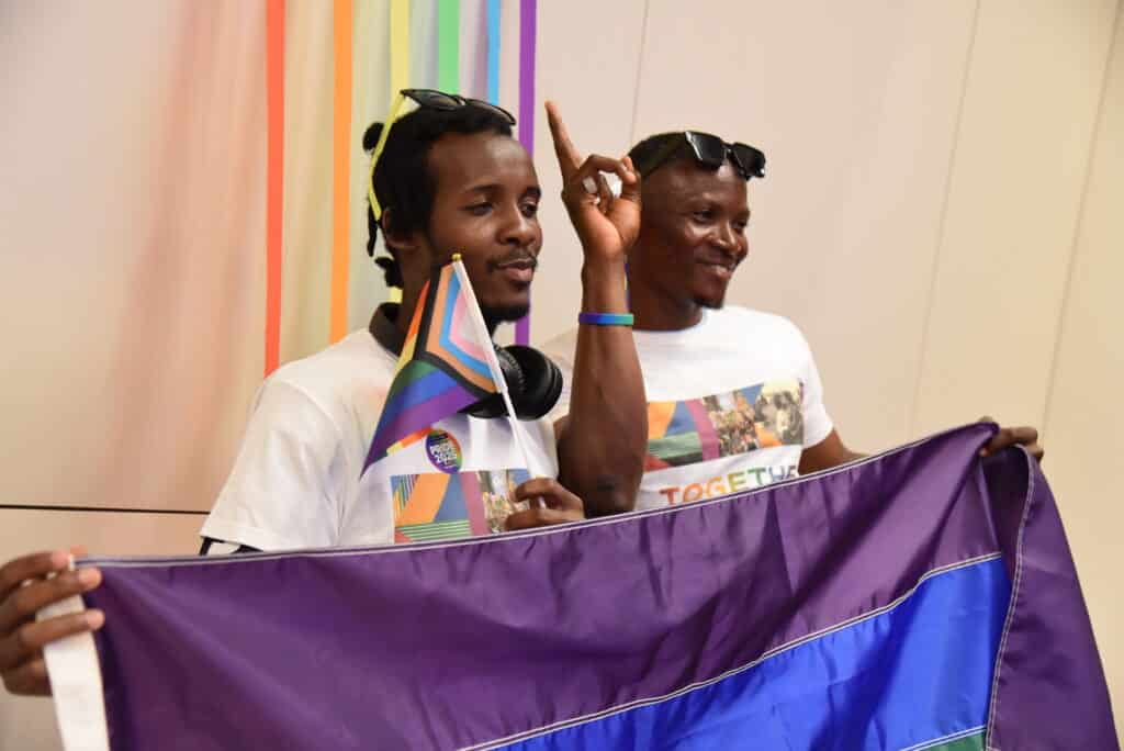 Two Black community members holding up a Pride flag while posing for a photo at The NYC LGBT Community Center. 