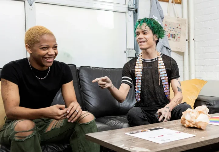 A group of two queer LGBTQ+ youth sitting at a table laughing at a TGNC transgender social group