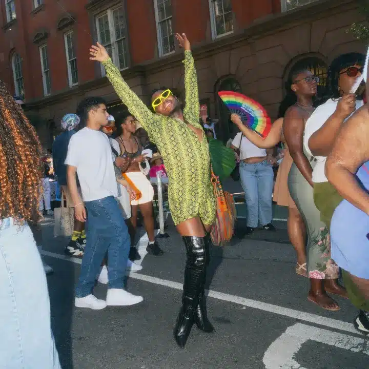 Queer person smiling with hands up at block party